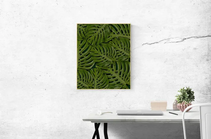 A desk with a framed monstera leaf print on the wall above it